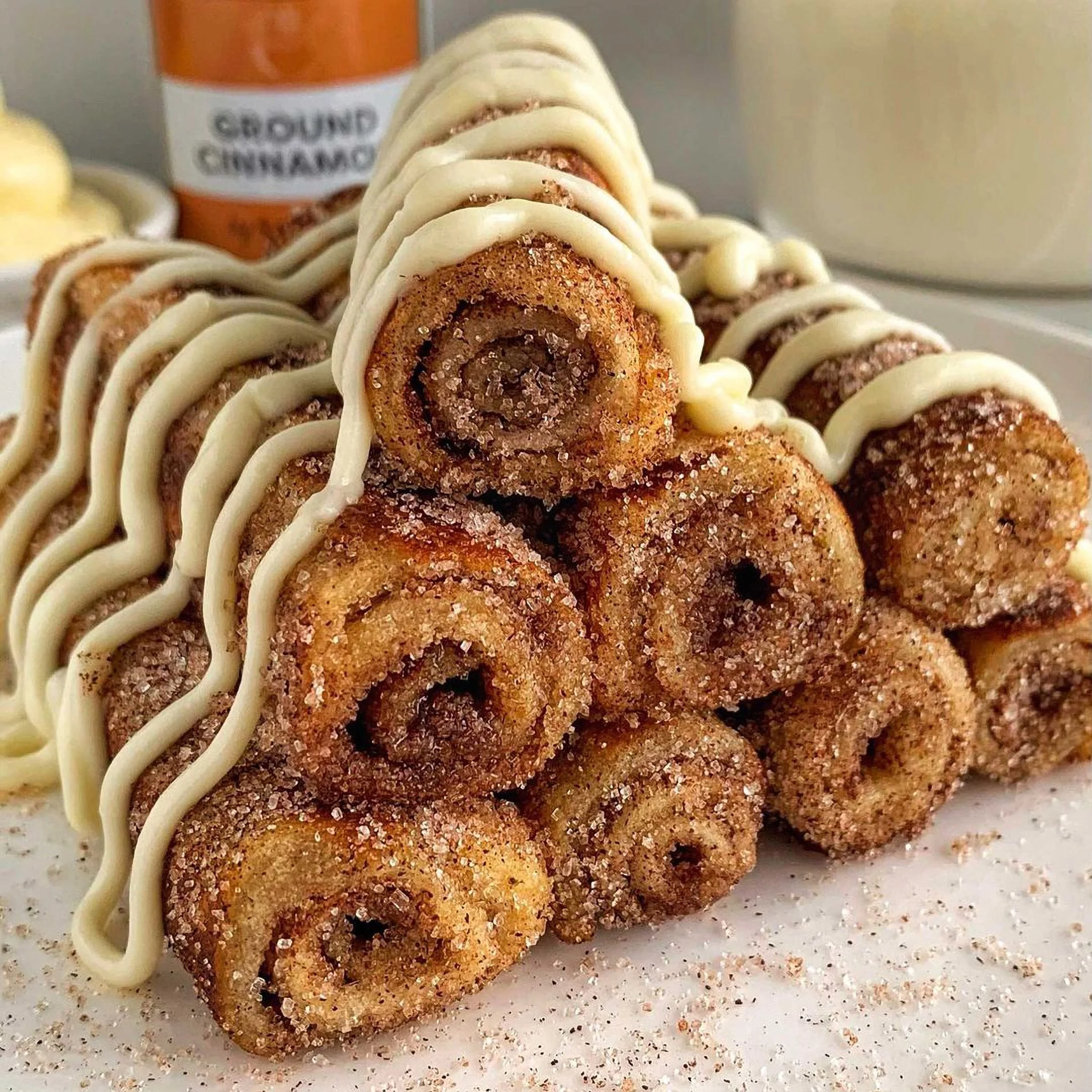 A stack of cinnamon roll French toast bites drizzled with cream cheese frosting and sprinkled with cinnamon sugar.